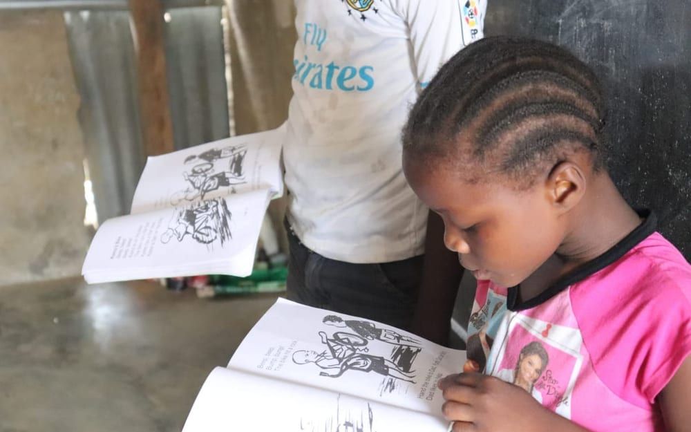 A teacher and community members working with a young learner at an outdoor desk